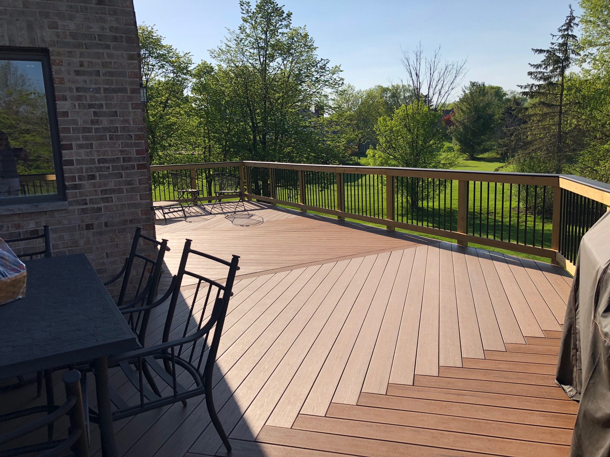 A large, multi-level composite deck with two-tone brown decking planks and black railings, offering ample space for outdoor living.